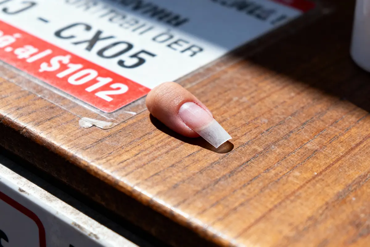 Faux ongle posé sur une table en bois, près d'une étiquette partiellement visible.