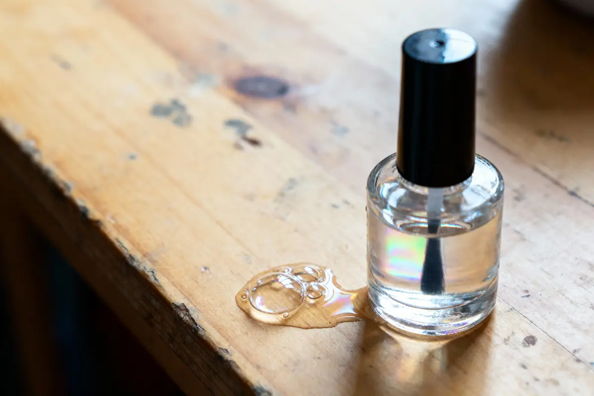 Flacon de vernis renversé, liquide transparent répandu sur une surface en bois.