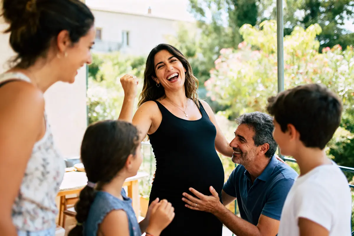 Personnes célébrant une grossesse, femme enceinte souriante entourée de famille, extérieur ensoleillé, ambiance joyeuse et chaleureuse.