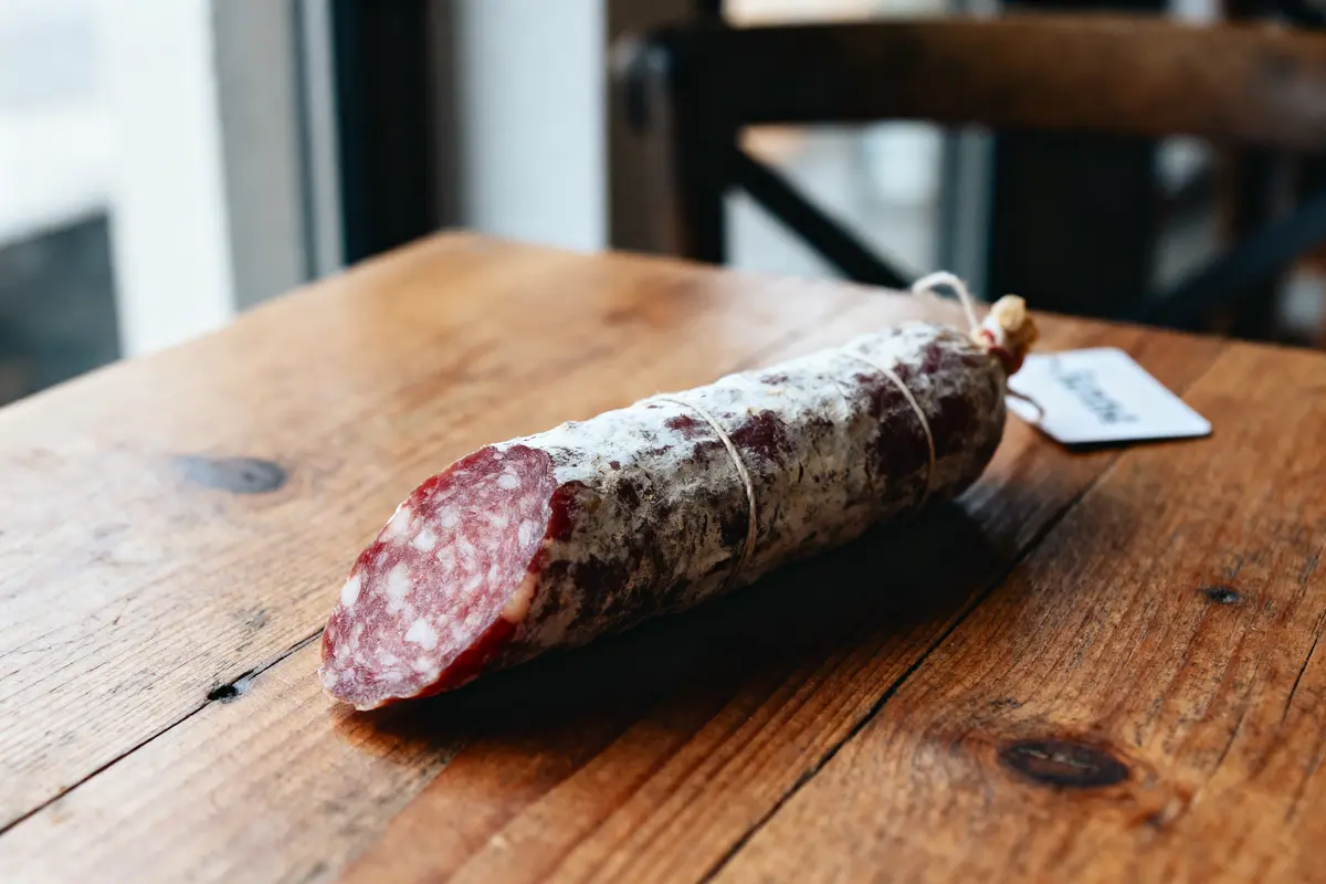 Un saucisson sec reposant sur une table en bois, étiqueté, près d'une fenêtre.