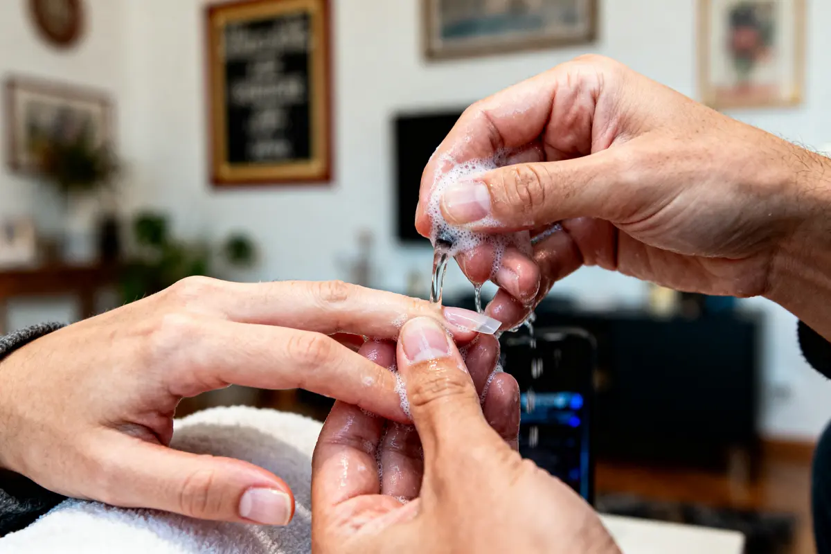 Manucure en cours avec mains féminines, application de gel et mousse savonneuse, arrière-plan flou et décor intérieur.