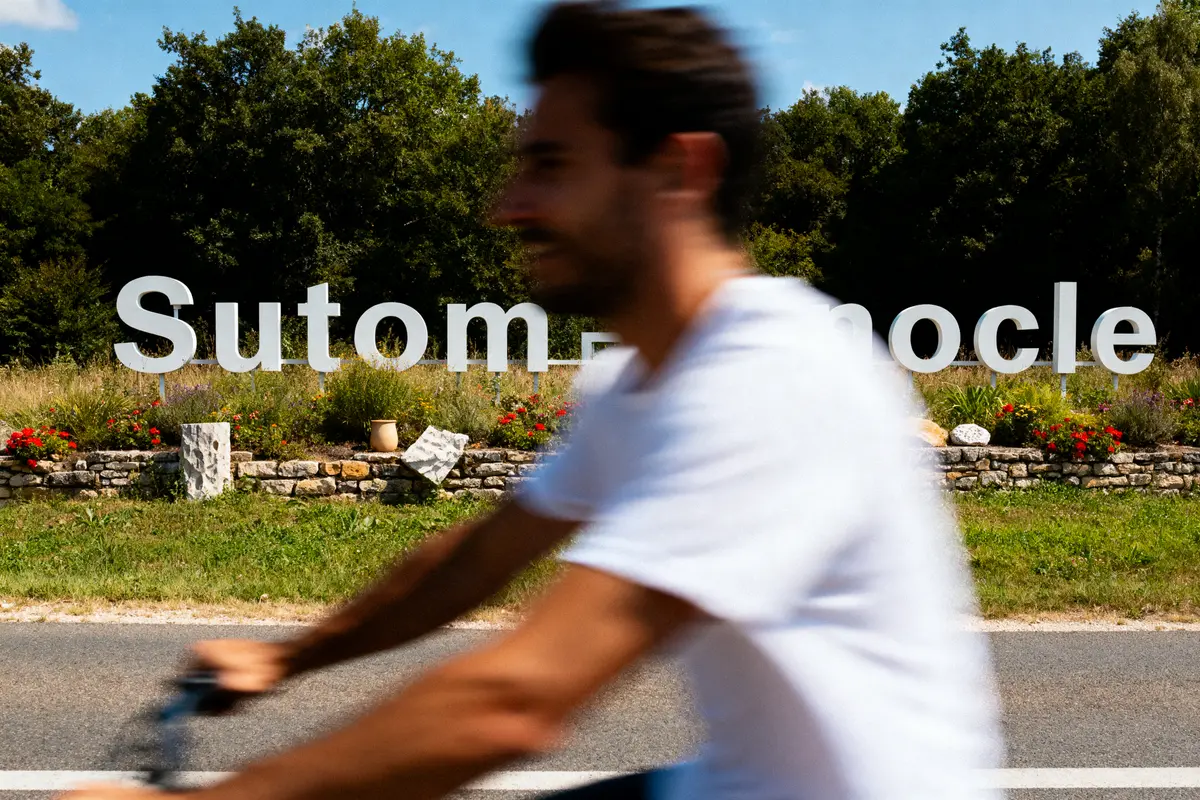 Homme flou à vélo devant un panneau flou avec arbres en arrière-plan.