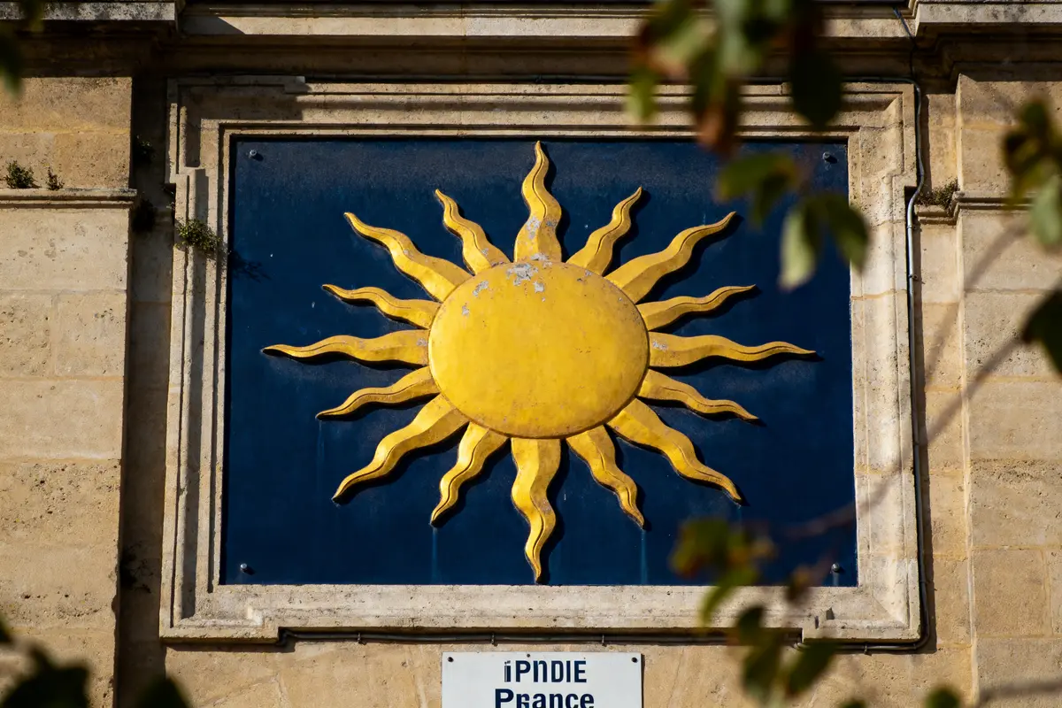 Relief soleil jaune sur fond bleu, encadré de pierre beige, panneau en bas clair-obscur.