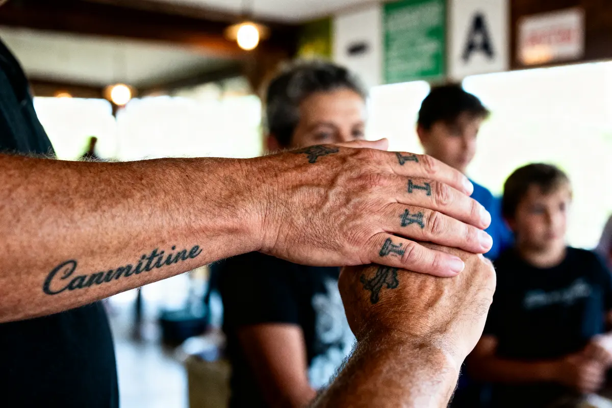 Gross plan de mains tatouées se serrant dans un environnement intérieur, avec des personnes floues en arrière-plan.
