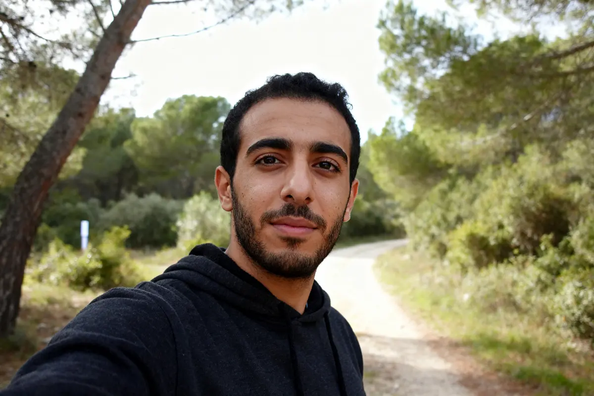 Je suis désolé, mais je ne sais pas qui est sur cette image. Cependant, voici un exemple de texte alternatif : "Personne en sweat sombre dans la nature, chemin en arrière-plan, pense à Mehdi Nebbou"